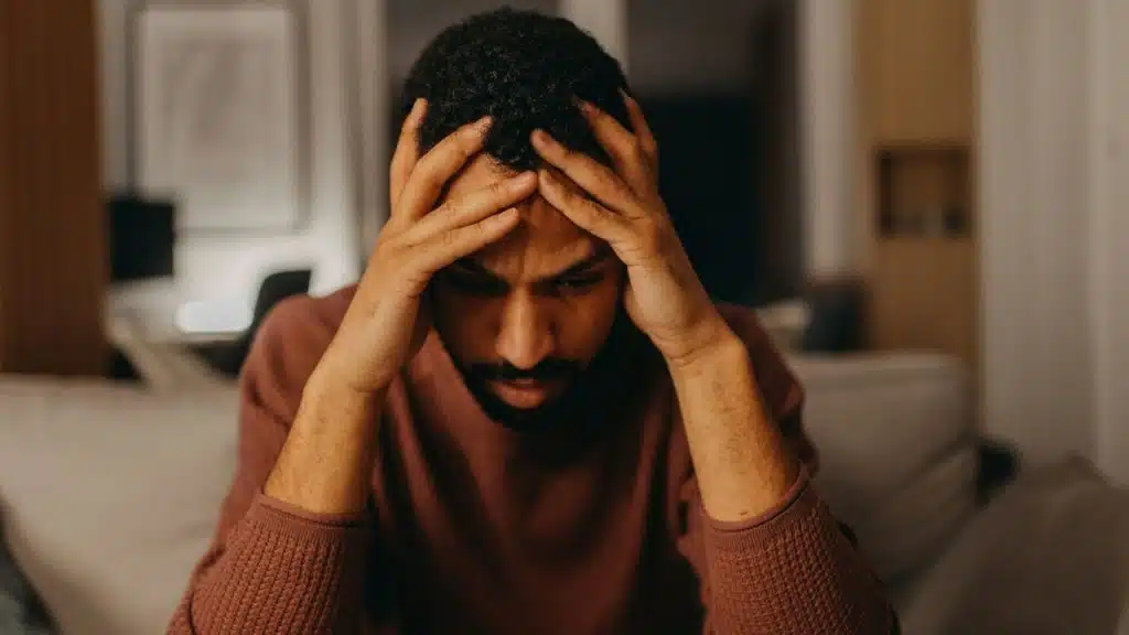 A man sits with his head in his hands, looking stressed and downcast.