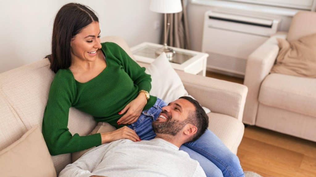 A happy man lies with his head on a woman's lap, and they look at each other and smile.