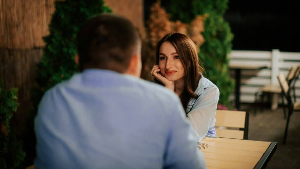 A woman resting her chin on her hand while looking at a man across a table.