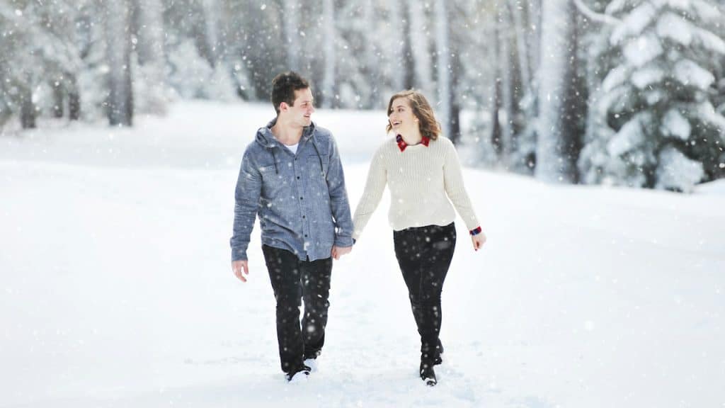 A couple walking on snow near trees during daytime.