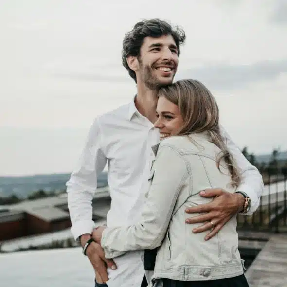 A couple smiling and hugging on top of a building.