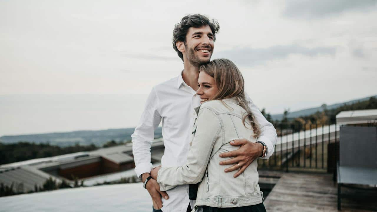 A couple smiling and hugging on top of a building.