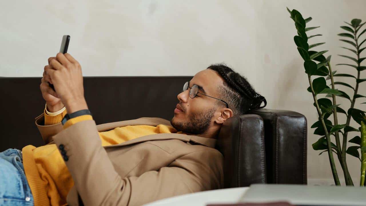 A man is lying on a couch while looking at his phone