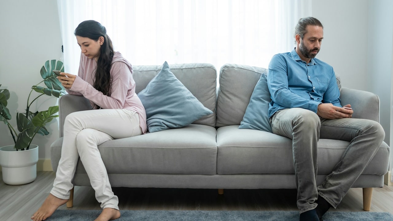 A couple sitting apart from each other on a couch and using their smartphones.