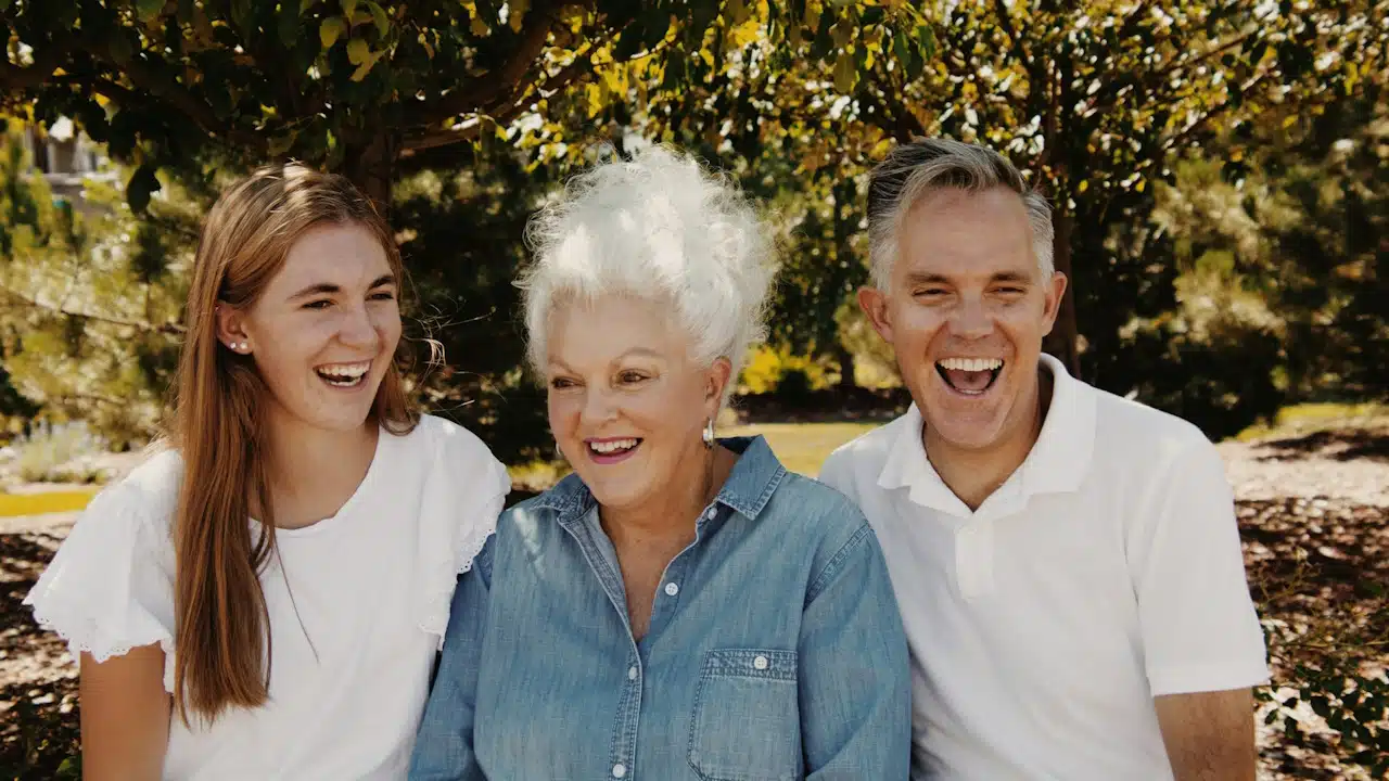 An older couple laughing along with their young daughter outdoors.