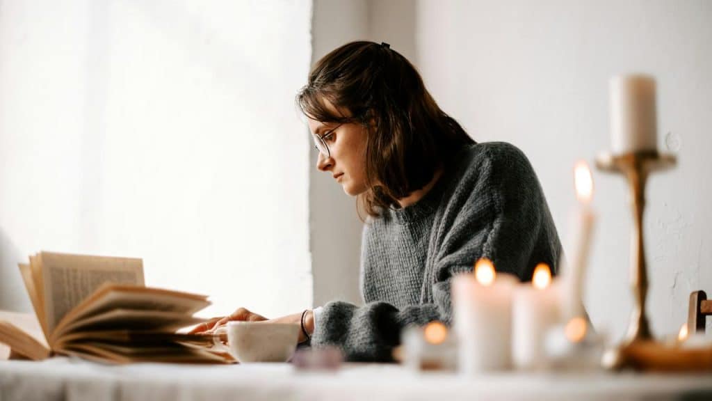 A woman reading a book at a table with lit candles.