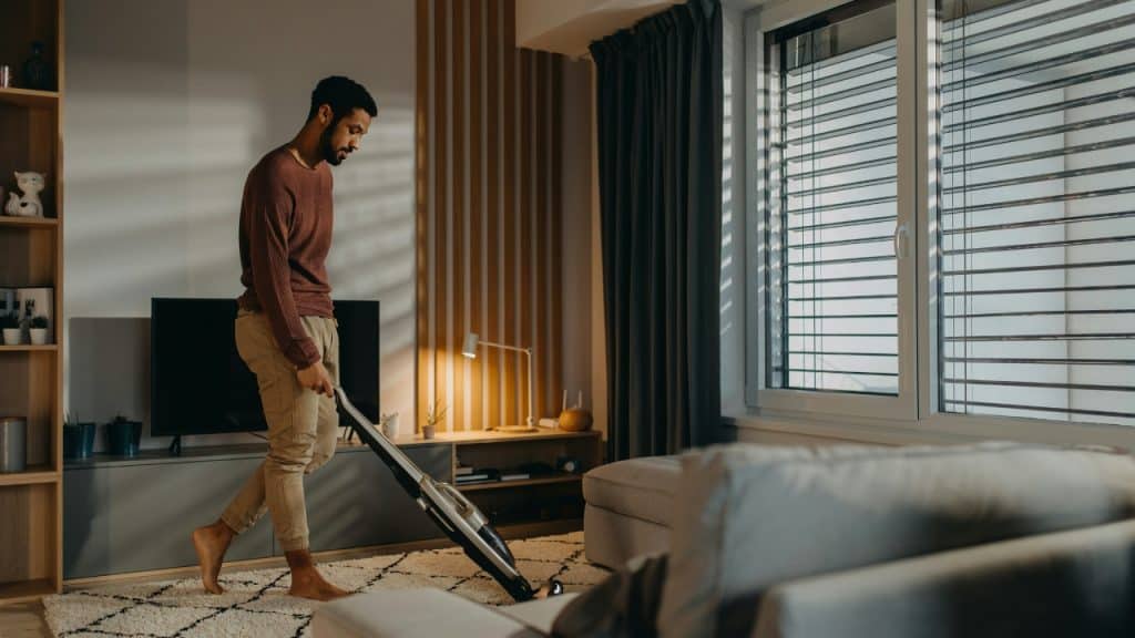 A man uses a vacuum cleaner to clean the carpet in a living room.