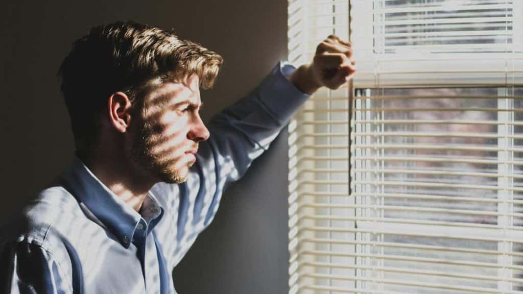 A man standing by a window with blinds.