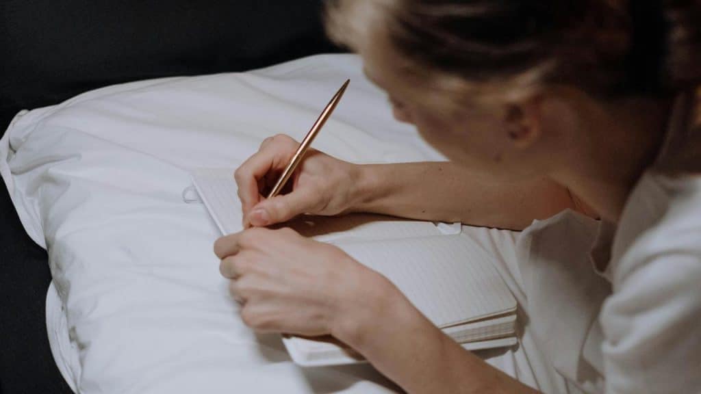 A person writing in a notebook on a bed.