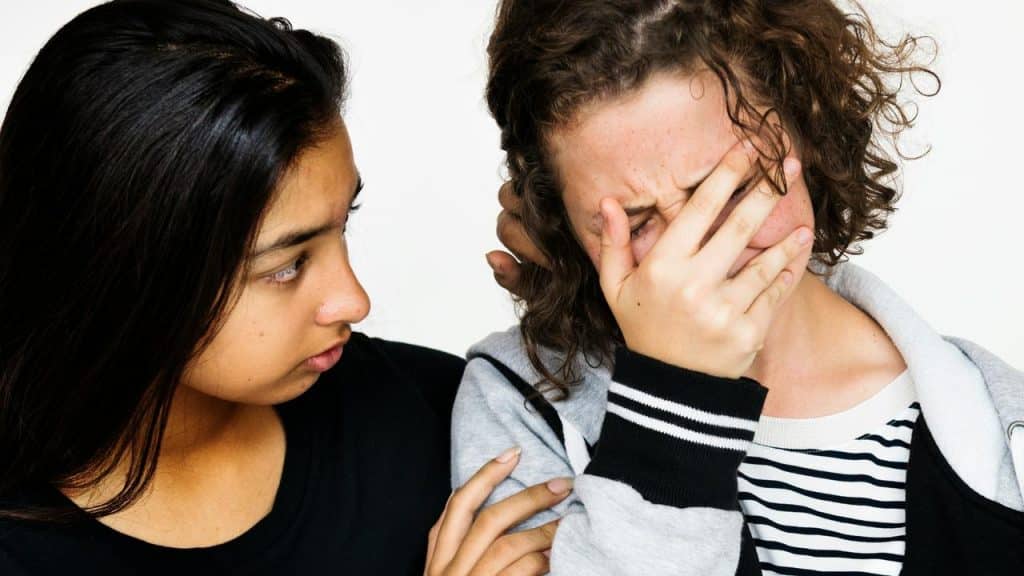 A woman comforting a crying friend covering her face.