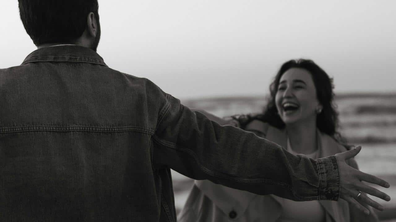 A man with open hands standing in front of a laughing woman who is coming towards him.