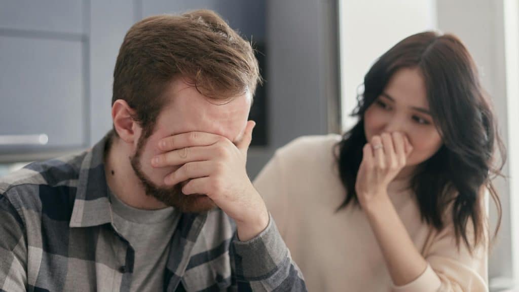 A man covers his face with his hand while a woman looks at him.