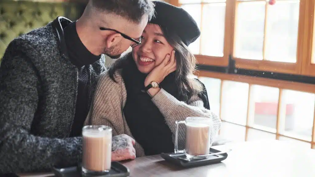 A couple sitting at a café, smiling and leaning close together.