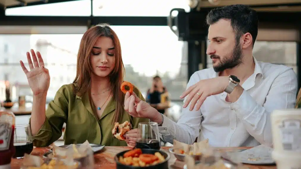 A man and woman sit at a table with food while looking away from each other.