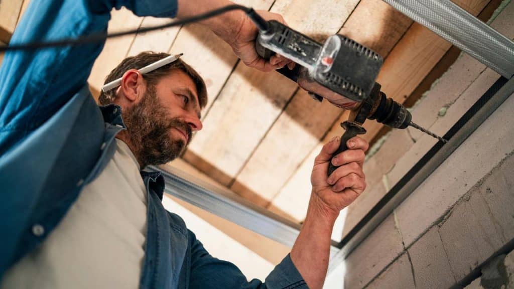 A man using a power drill overhead while working on a construction project.