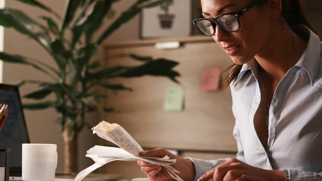 A woman wearing glasses reviewing receipts at a desk