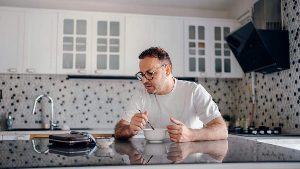 A man sitting at a kitchen counter eating from a bowl.