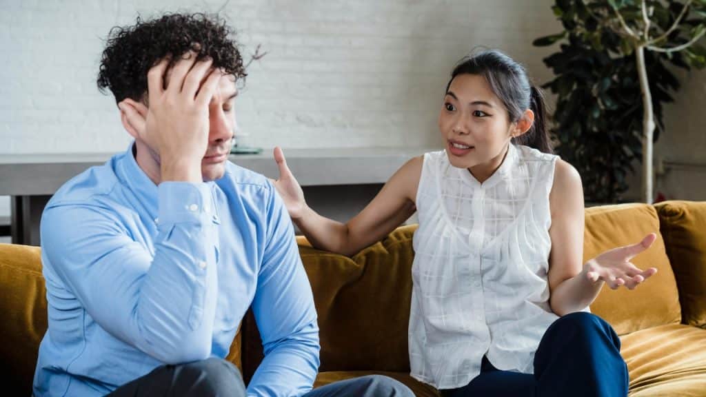 A woman gestures while speaking to a man who is holding his hand to his head.