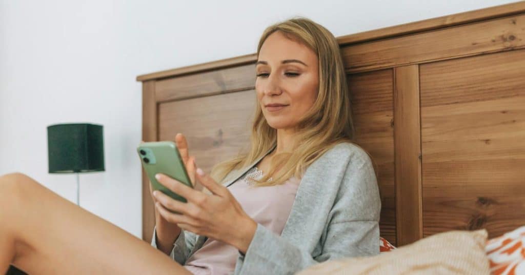 A woman relaxing on a bed while looking at her smartphone.