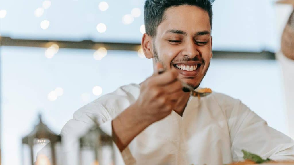 A smiling man enjoying a meal indoors with a spoon in hand.