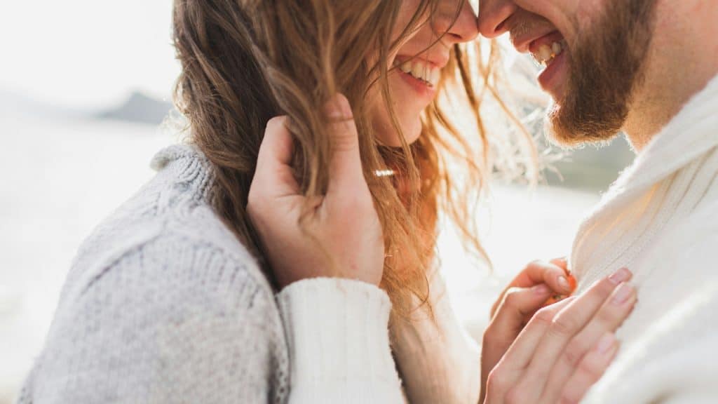 A woman touches her hair while smiling closely at a man face-to-face.