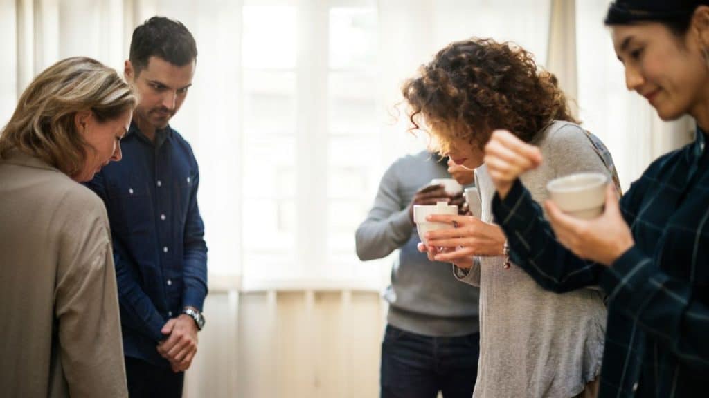 A group of people stand in a circle holding cups while looking down or away.