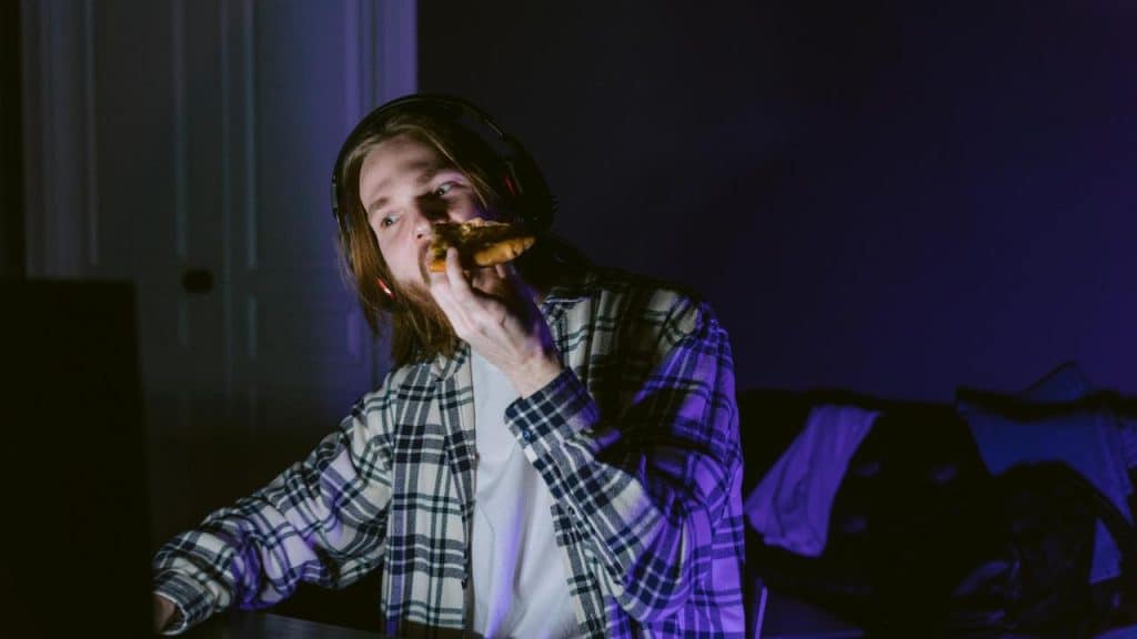 A man wearing headphones eating pizza in a dimly lit room.