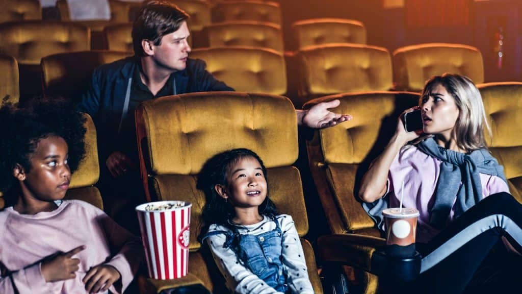 Woman talking on the phone in the cinema and showing a rude gesture at the man behind her.