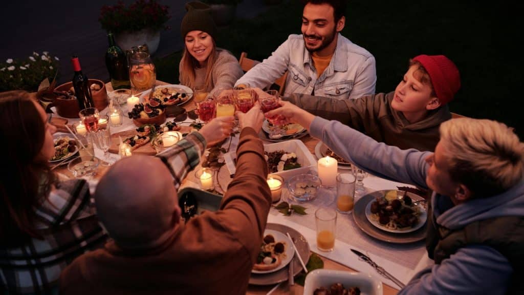 A group of friends sits around an outdoor dinner table toasting with drinks.