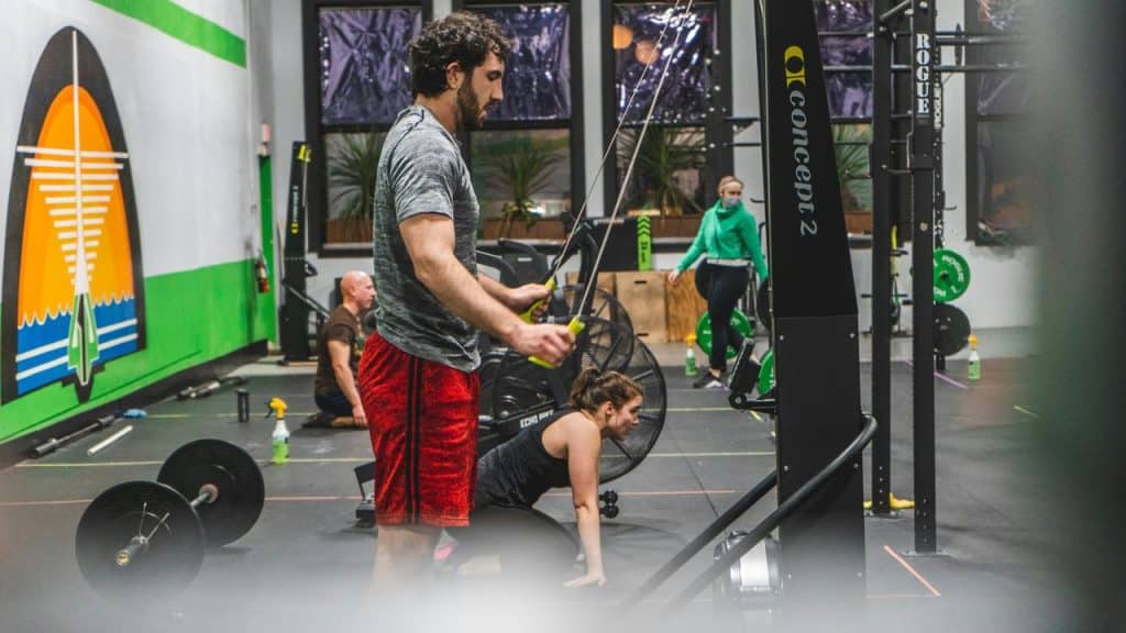 A man using a cable machine in a gym while others exercise nearby.