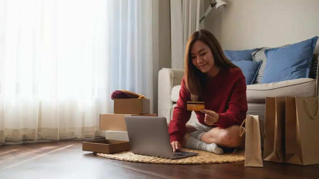 A woman shopping online with a laptop and credit card at home.