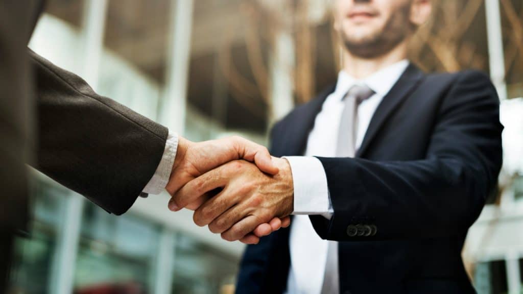 A close-up of two people in business suits shaking hands in an office setting.