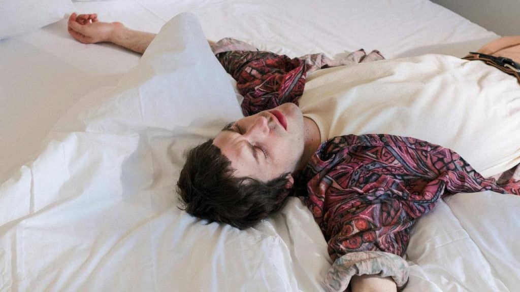 A man lying on a bed with his arms spread out and eyes closed.