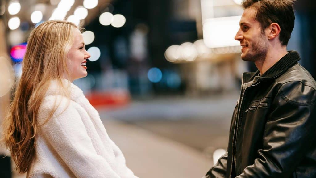 A smiling couple standing and talking on a city street at night.