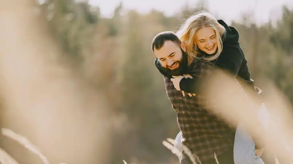 A man gives a woman a piggyback ride, and both are smiling brightly.