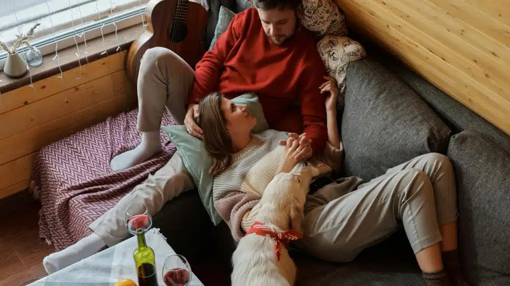 A cozy couple relaxing on a couch with their dog.