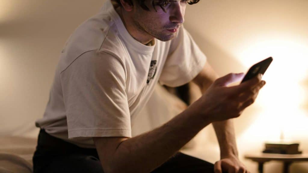 A person sitting on a bed and looking at a smartphone.
