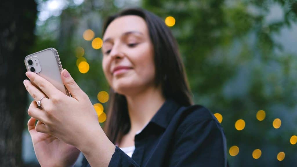A woman using her phone outdoors with lights in the background.