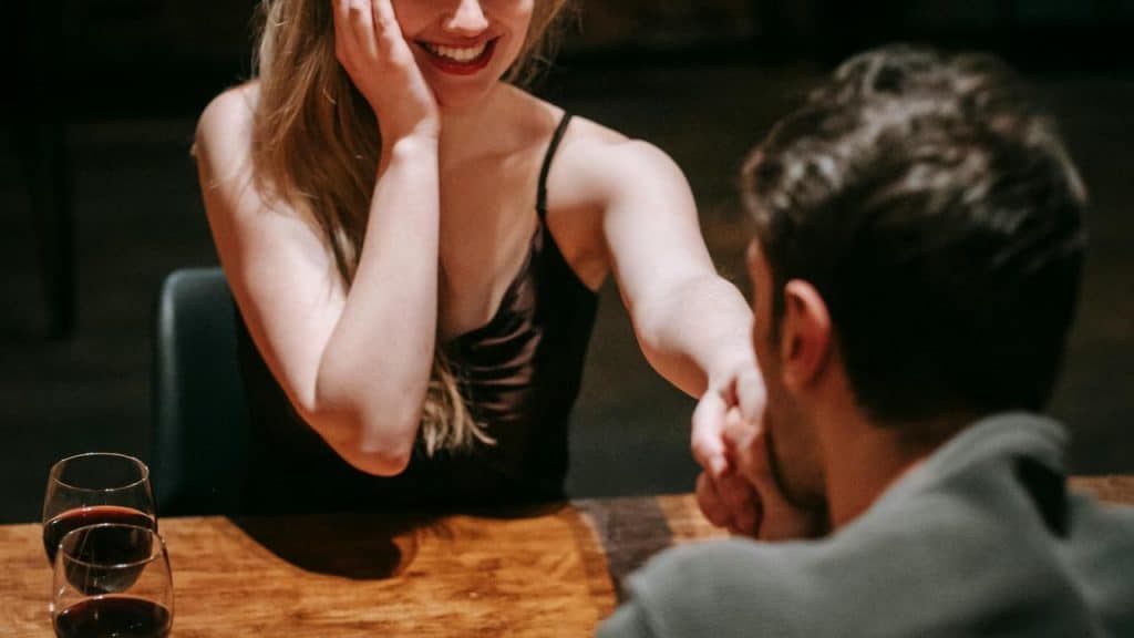 A woman smiling while holding a man’s hand across a table.