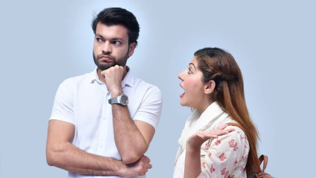 A man looks away thoughtfully while a woman speaks to him with open hands.
