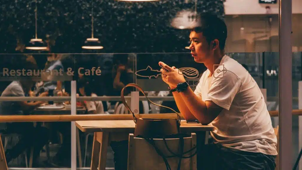 A man sitting at a restaurant table looks at his smartphone in the dark.