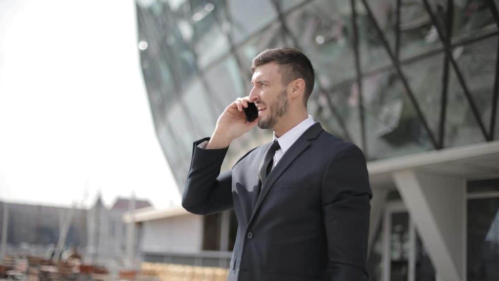A man in a suit talking on a phone outside a modern building.