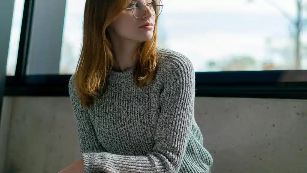 A woman wearing glasses and a gray sweater looks to the side