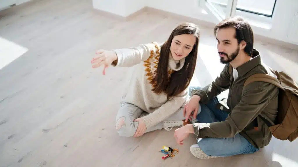 A woman sits on the floor and points while a man sits beside her.