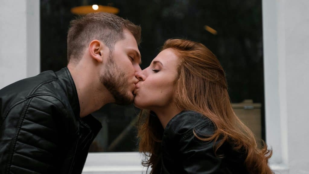 A man and woman in black leather jackets kissing against a plain white background.