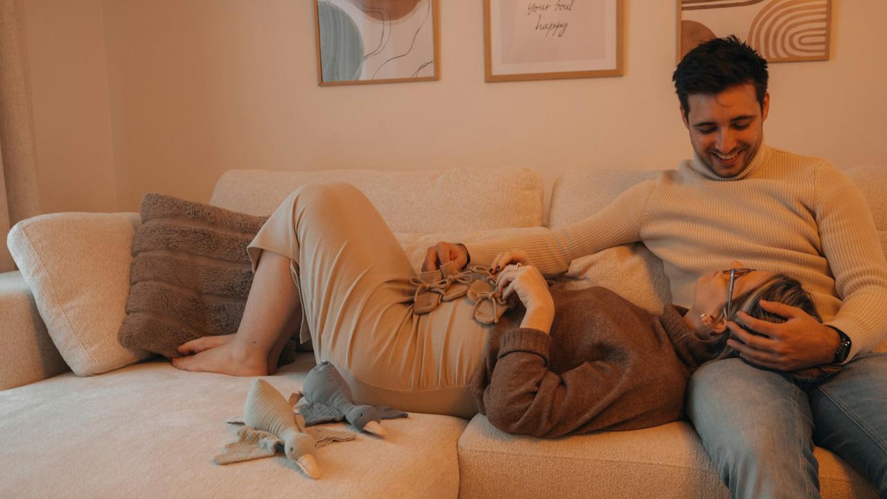 A woman lying on a couch with her head in her smiling partner’s lap.