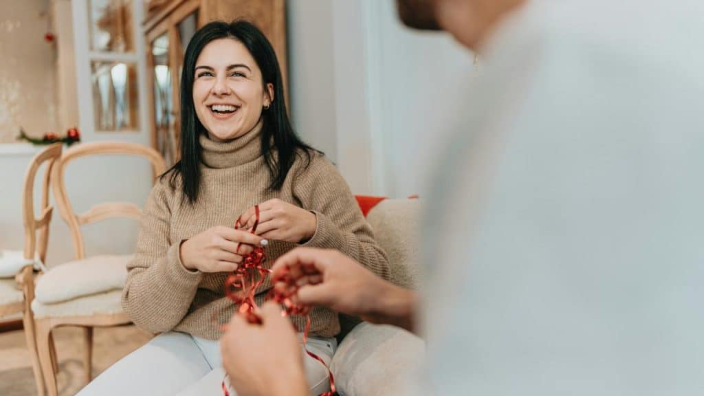 A smiling woman sitting indoors while holding red ribbon during a conversation.