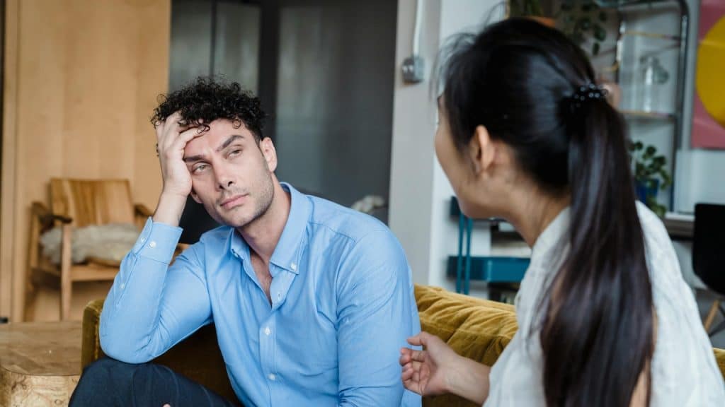 A man sits with his hand on his head, listening to a woman talking.