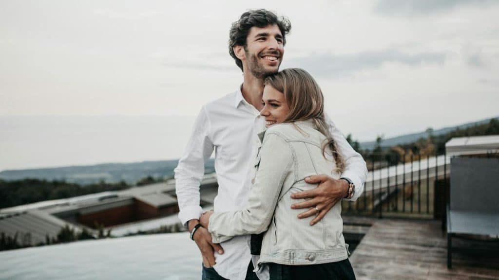 A smiling couple hugging each other while standing on the top of a building.