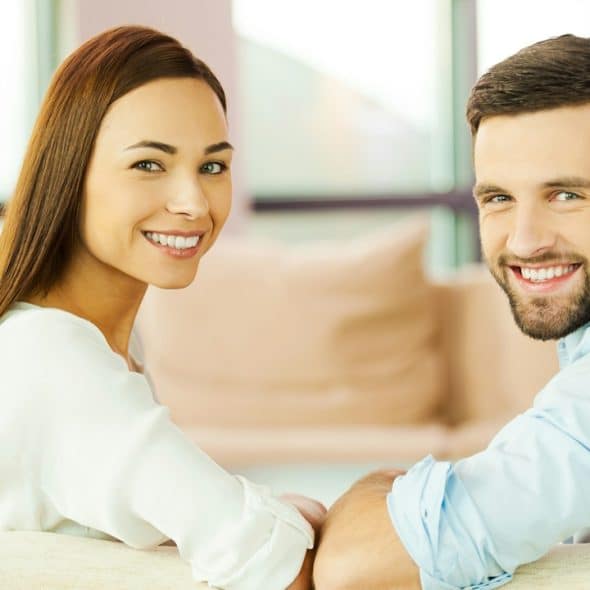 Rear view of a beautiful, young, loving couple sitting together on the couch and smiling.